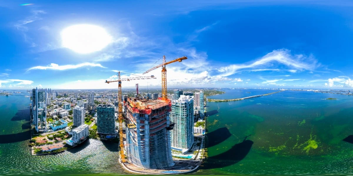 Vista aérea de una torre residencial en construcción con grúas, frente a la bahía de Miami