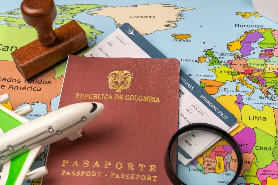 Pasaporte colombiano junto a un avión de juguete, un sello y tarjetas de embarque sobre un mapa