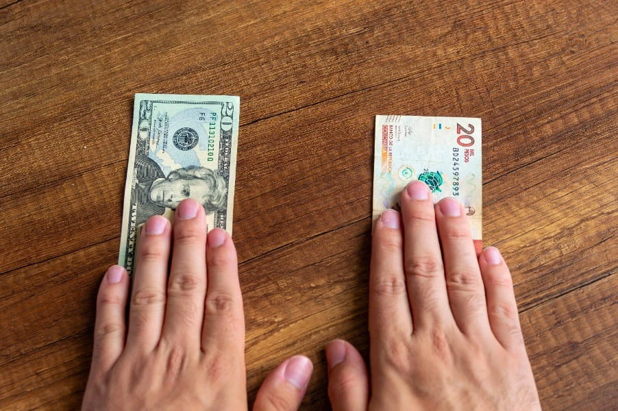Dos manos sobre un billete de 20 dólares y otro de 20.000 pesos colombianos