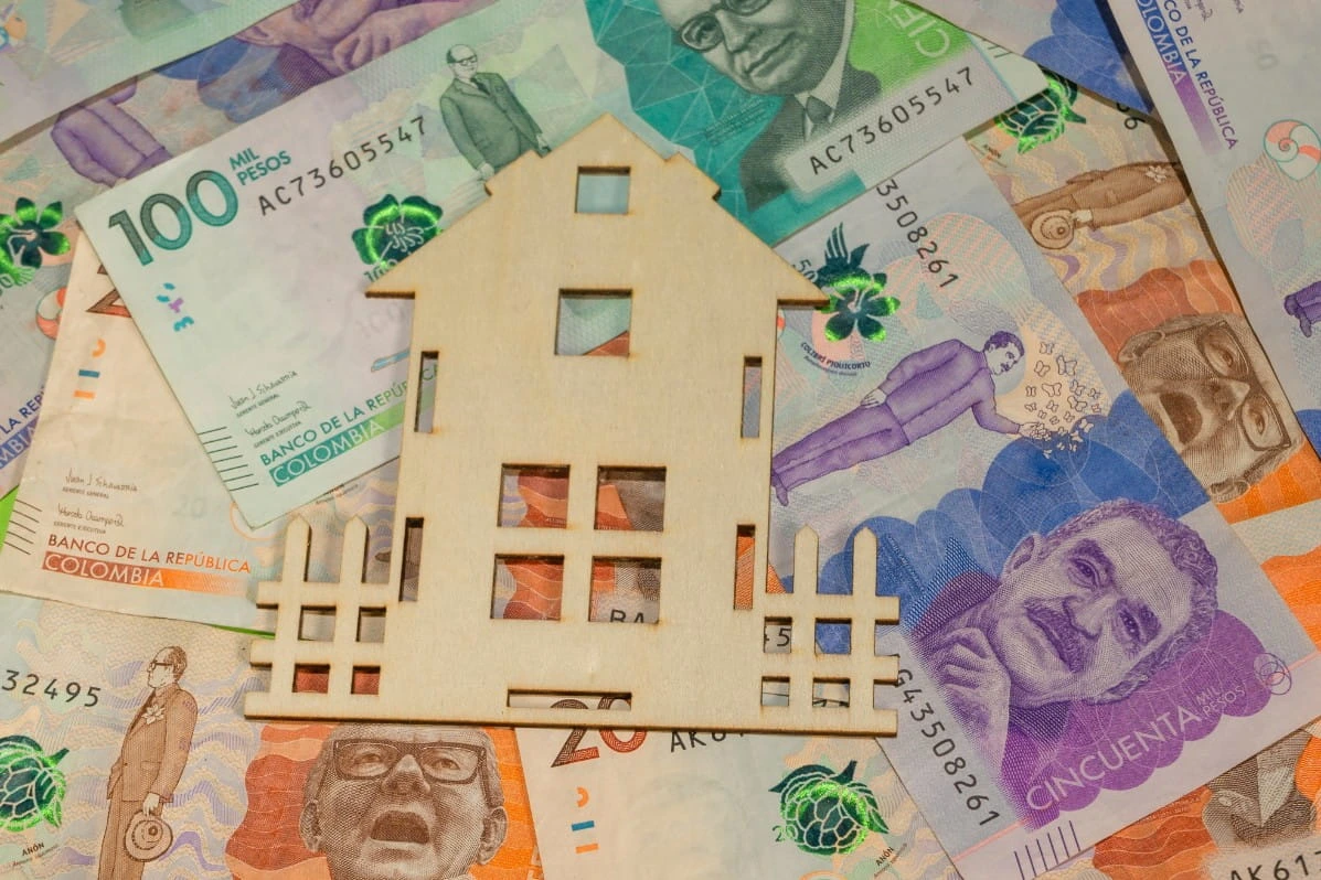 Casa de madera en miniatura sobre billetes colombianos de 100.000, 50.000 y 20.000 pesos