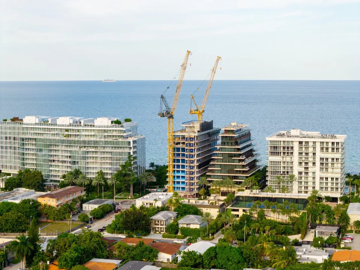 Vista aérea de edificios frente al mar en el sur de Florida, con una torre residencial en construcción entre dos grúas