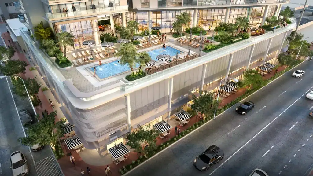 7200 Collins — vista aérea de la terraza de amenidades sobre el podio: piscina estilo resort rodeada de camastros y sombrillas, palmeras, jardineras y un salón acristalado al fondo, con Collins Avenue abajo a la derecha