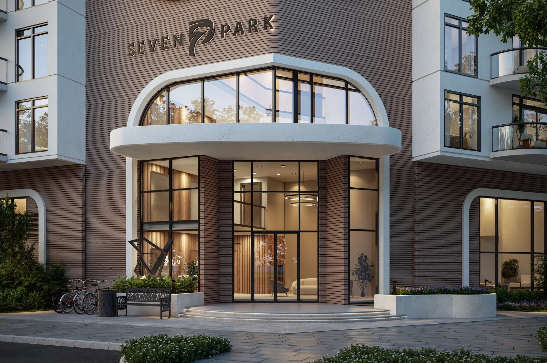 Seven Park Residences — acceso principal iluminado bajo el letrero SEVEN PARK, con parqueo de bicicletas junto a la entrada