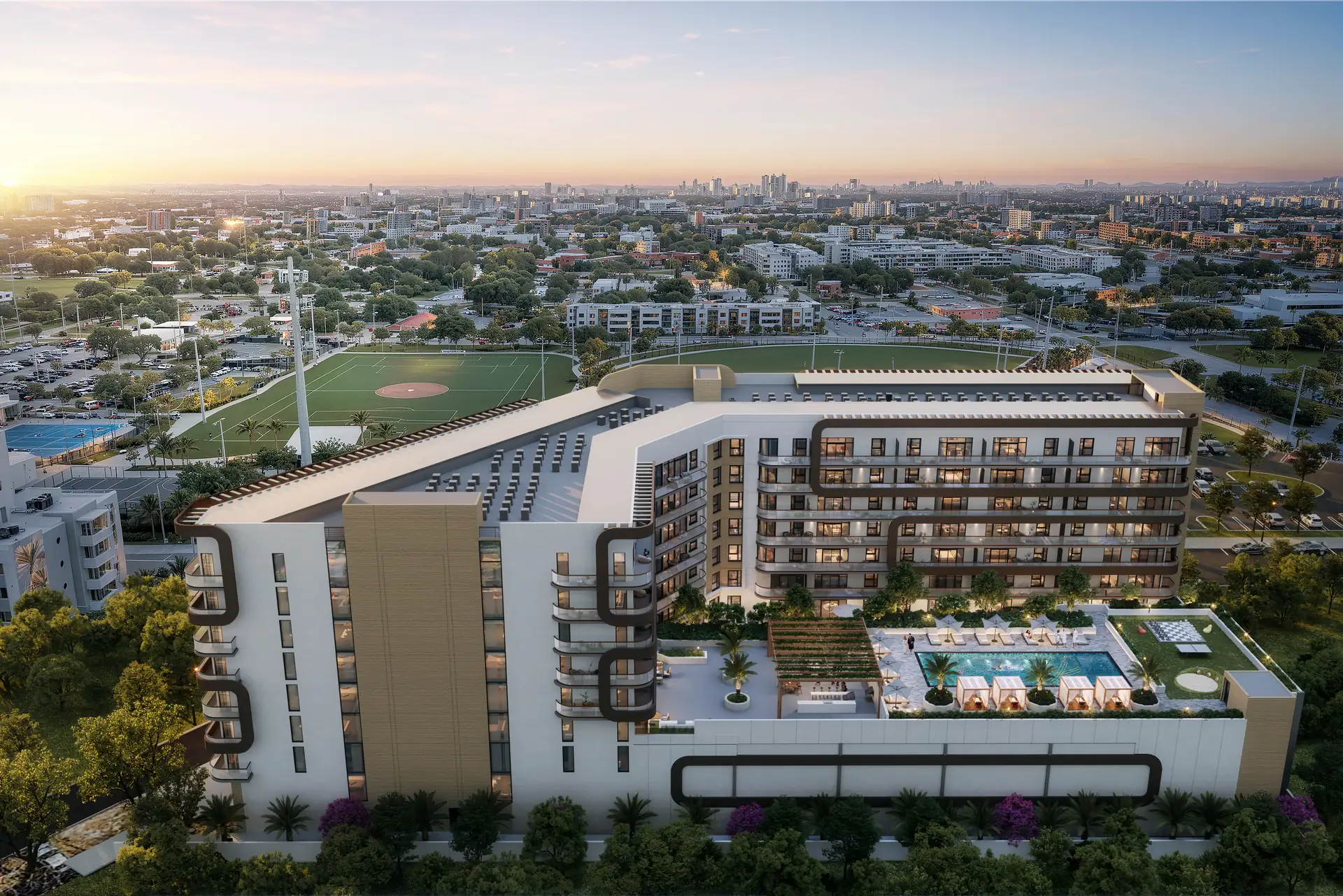 Seven Park Residences — vista aérea del edificio al atardecer, con la terraza de piscina sobre la base y el parque con campos deportivos al frente