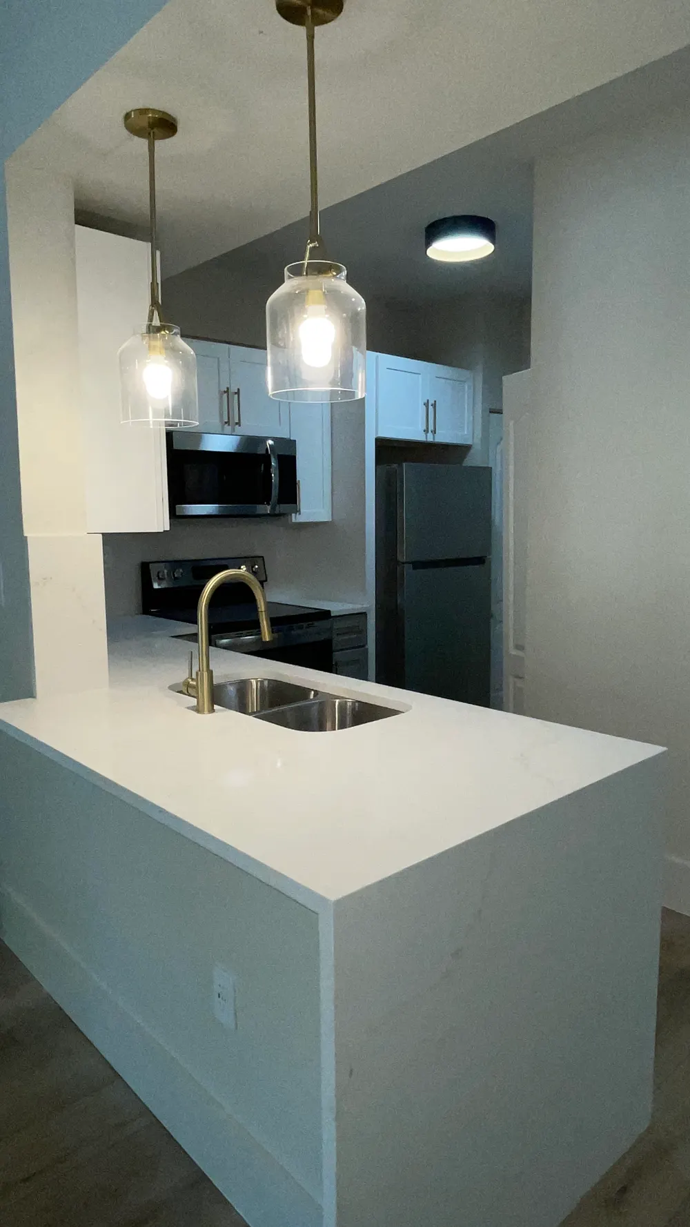 Valencia South Miami — cocina renovada con isla de cuarzo, gabinetes blancos y electrodomésticos de acero inoxidable, ejemplo de una residencia renovada